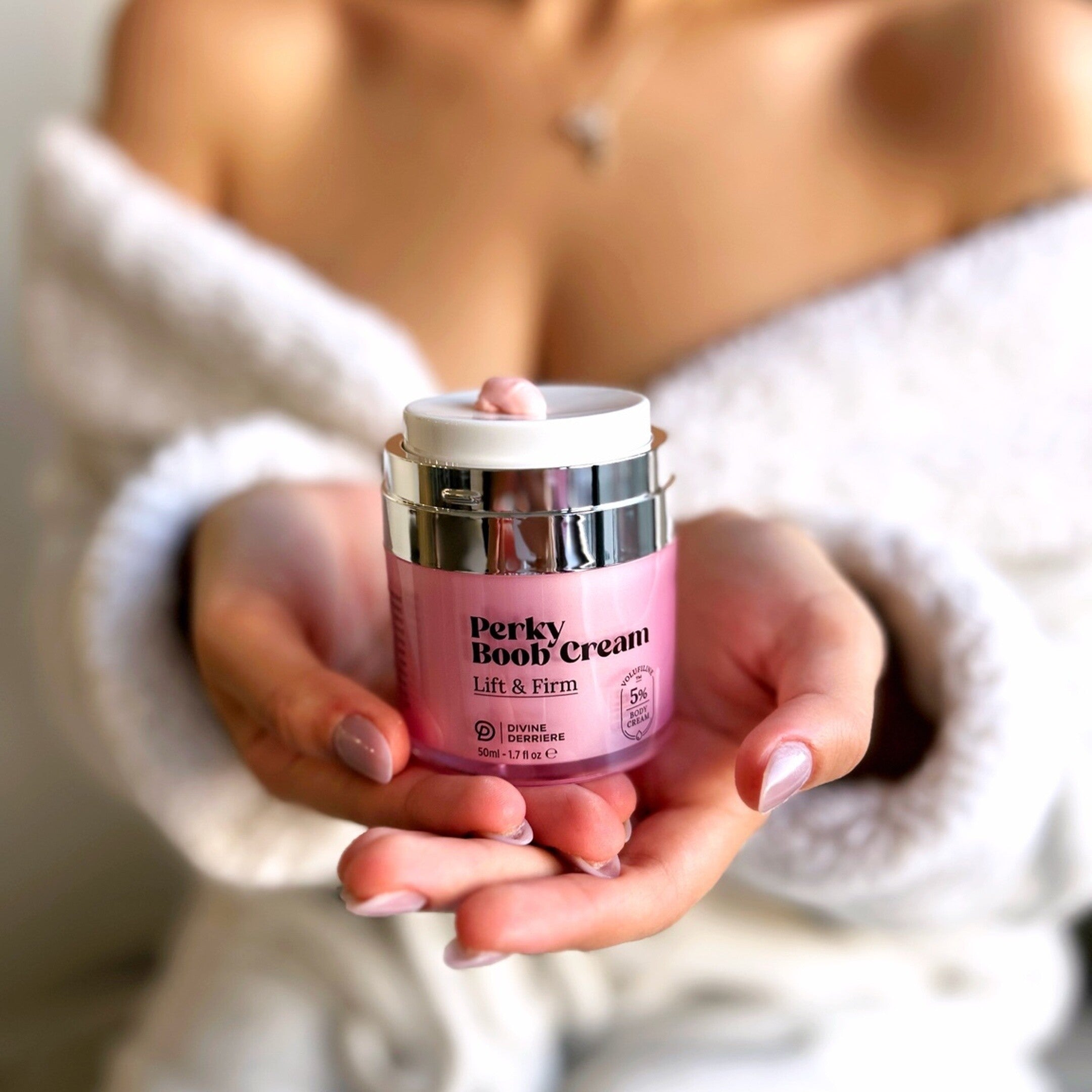 Divine Derriere Perky Boob Cream held in hands, with pink cream on the pump